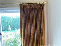 Brown velvet curtain panel fully covering a wide window with metal rods visible at top.