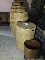 Image showing a lineup of several woven baskets of different sizes and shapes with a metal kindling holder in front next to a stone fireplace.