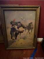 Photo of framed print showing cowboy on horseback, dusty and worn frame.