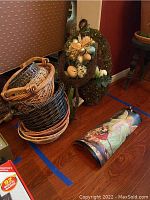 Photo of seven decorative baskets stacked inside one another with an Easter wreath with greenery and colored faux eggs behind them on the floor near a wall.