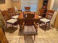 Six wood dining chairs around a wood dining table, including two captain chairs and four side chairs with cushions at the seats.