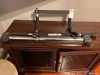 Pull up bar folded and resting horizontally on wooden cabinet, showing foam grips and adjustable metal bar