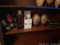 Shelf with seven opening black resin picture frame, Bombay-style clock, Scentsy kit in box, pair of large decorative eggs on stands, and rectangular decorative box with damage.