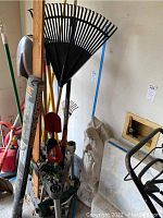 Photo showing various garden tools including rakes with black plastic tines, shovel, hoe, and the plastic organizer stand holding tools upright
