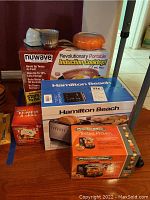 Overview of all boxed kitchen appliances and items including Proctor Silex food chopper, Hamilton Beach toaster, Nuwave induction cooktop, EZ Press n Grill, 6 ramekins, and pumpkin