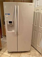 Front view of the Samsung side-by-side refrigerator showing white doors, handles, and front dent.
