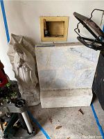 Tombstone piece with irregular stone-faced front leaning against wall next to concrete Virgin Mary statue in garage environment.