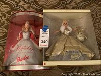 Two boxed Barbie dolls side by side: 2000 Celebration Barbie in gold and white outfit and 2001 Holiday Celebration Barbie in silver and white dress with tiara.