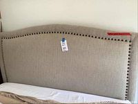 Front view of beige upholstered headboard with nailhead trim and part of mattress