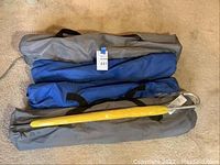 Four outdoor camp chairs packed in their colored carry bags placed on a carpeted floor, including two gray, one bright blue, one dark blue bag.