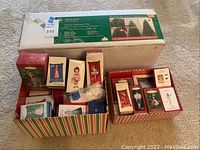 Photo showing GE Deluxe Series 4.5 ft pre-lit artificial Christmas tree box with two boxes of boxed Barbie keepsake ornaments containing multiple ornaments each.