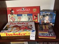 Photo showing Mickey Mouse Monopoly game, Twister game, Disney puzzle, and USC tin box arranged together on a shelf.