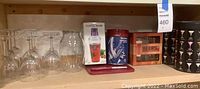 Shelf display showing six wine glasses, large pitcher, boxed cocktail shaker, boxed martini glass set, and a tin or box with barrels graphic.