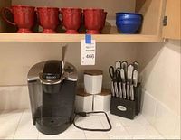 Photo of Keurig coffee maker, Ginsu knife set with block, and three ceramic canisters with wooden lids on a kitchen counter.