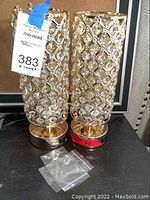 Two gold colored desk lamps with faux crystal latticed shades shown together on a black surface. Extra crystals included in a small plastic bag in front of lamps.