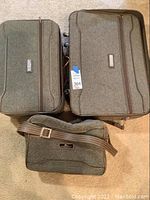 Three-piece luggage set shown from top with all pieces visible: large suitcase with wheels, medium suitcase, and shoulder bag.