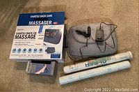 Photo shows Felicity Shiatsu back massager with power adapter, boxed foot massager, and two rolls of clear contact paper on carpet.