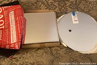 The set of eight 12x12 inch square beveled mirrors stacked or packed, partially wrapped in paper with a red bag nearby, showing clean mirror edges and surfaces.