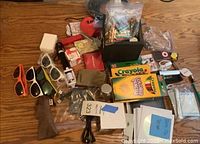 Photo showing assortment of office supplies including eyewear, crayons, colored pencils, iPod, cords, pouches, and paper items laid out on a wooden table.