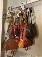 Lot of seven purses mostly hanging on hangers and a rack, various styles and materials