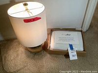 Photo showing the lit brass colored table lamp and boxed Pura Sleep travel pillow on carpet.