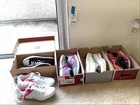 Four pairs of athletic shoes in their boxes and one pair out of box. Sizes 8 and 8.5 indicated. Used condition.