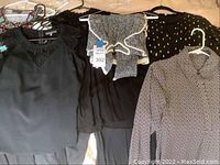 Four women's dressy blouses and one knit sweater laid out, showing different patterns and styles including black sleeveless blouse and knit sweater.
