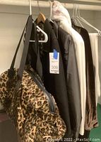 Leopard print duffel carryall bag hanging on a rack next to women's trench coats and scarves.