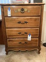 Full front view of the four-drawer light wood dresser showing decorative handles and floral design on top drawer.