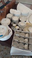 Full overview of the table with stacked and packed dinnerware pieces including plates, bowls, cups, and zippered covers.