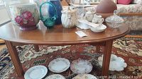 View of entire wooden coffee table showing smooth top surface with contents (not included) on top and decorative plates on the floor beneath.