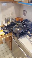 Assorted cookware on countertop including stainless steel pots, frying pans, griddle pan, some with glass lids.