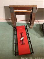 Overview photo showing one red padded Craftsman rolling creeper and one wooden saw horse with metal braces.