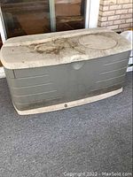 Front and top view of a gray and white Rubbermaid plastic deck box, dirty with visible stains and dirt marks on the lid and sides.