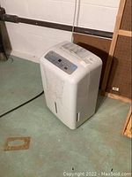 White GE dehumidifier on basement floor, front view with control panel visible.