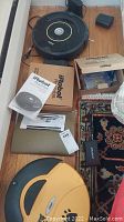 Overview of black Roomba vacuum, charging base, accessories box, manual, and small black remote case