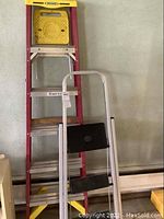 Full view of red fiberglass ladder with yellow top and separate black step stool.