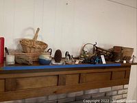 Wide view showing all items: woven basket, ceramic figures, wooden bucket, pinecone candle, bunny bank, and other small decor pieces on a mantle shelf.