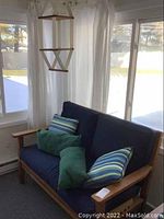 Wood framed loveseat with blue cushions placed in a window corner, pillows on cushions.