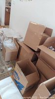 Multiple open and stacked cardboard boxes with some packing materials inside, seen on a carpeted floor near a kitchen.