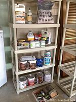 Photo of shelving unit with multiple cans of paint, bottles, and a bag of sand stored on shelves.