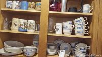 Multiple shelves of ceramic dinnerware including mugs, bowls, plates, and collectible mugs with various patterns. Predominantly Pfaltzgraff Blue Floral pattern pieces visible, stacked in multiple quantities.