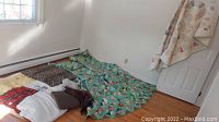 Wide view of quilts and blankets arranged on the floor near window and door, showing variety of patterns and textures.
