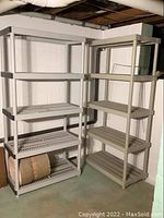 Two beige plastic shelving units placed side by side in basement near concrete block walls, each with four open slatted shelves and tubular legs.