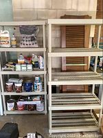 Two beige Keter plastic shelving units with slatted shelves, situated side by side with brown wooden doors leaning behind them. Various storage items visible on one shelf unit, but not included in lot.