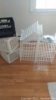 Photo showing stacked white plastic storage crates with lattice design and black plastic crate on top.