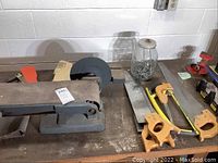 Photo showing Craftsman belt and disc sander along with saws, orange wooden pegs, jar of nails, and red vise.