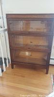 Front view of three-section oak barrister bookcase showing glass-front drop-down doors and overall finish