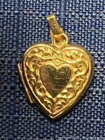 Front of 10kt gold heart-shaped locket pendant showing detailed scrollwork design with central smooth heart