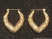Front view of both gold earrings showing twisted textured design and hoop shape on black background.